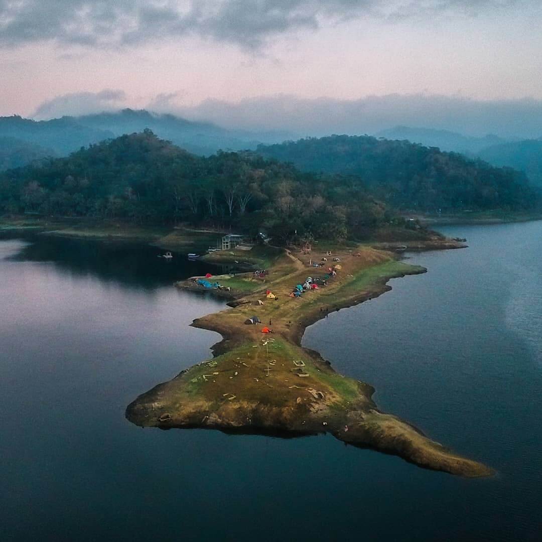 Aerial view of campers on a narrow strip of land surrounded by the waters of Sermo Reservoir at dusk.