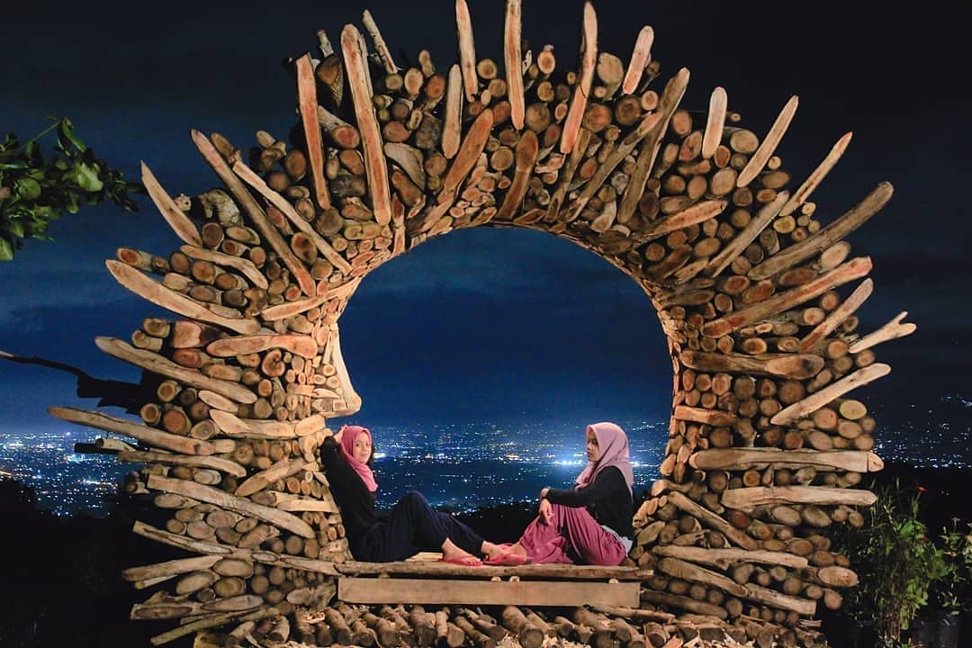 Two people sitting in a wooden circle structure at Mount Mungker with a nighttime city view in the background.