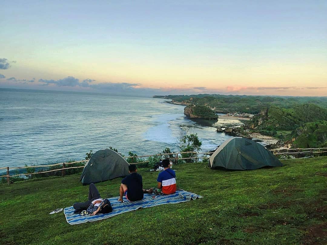 Campers relaxing on a grassy hill at Kosakora Peak, overlooking the ocean and coastline during sunset.