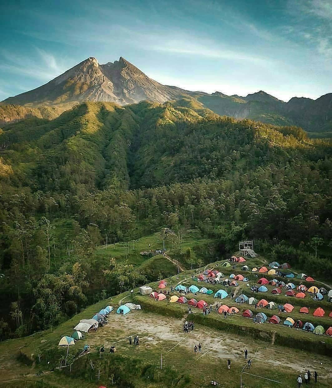 Aerial view of a campsite at Klangon Hill with rows of colorful tents and Mount Merapi in the background under a clear sky.