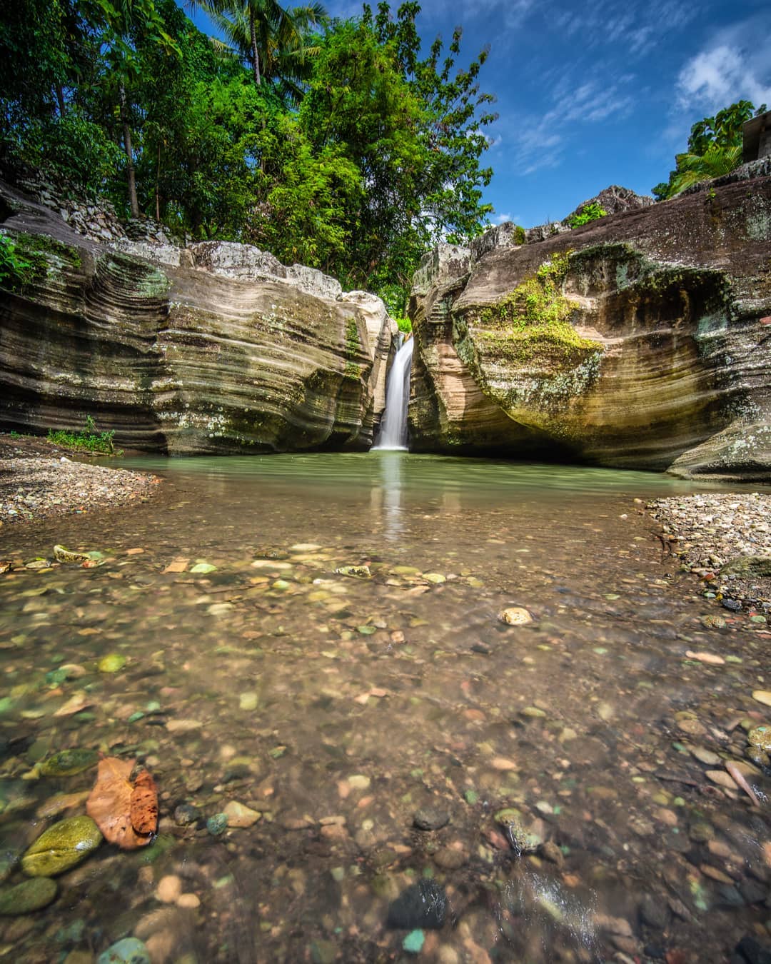 Luweng Sampang Waterfall with clear water flowing through unique limestone cliffs surrounded by lush greenery in Gunungkidul, Yogyakarta, Indonesia.