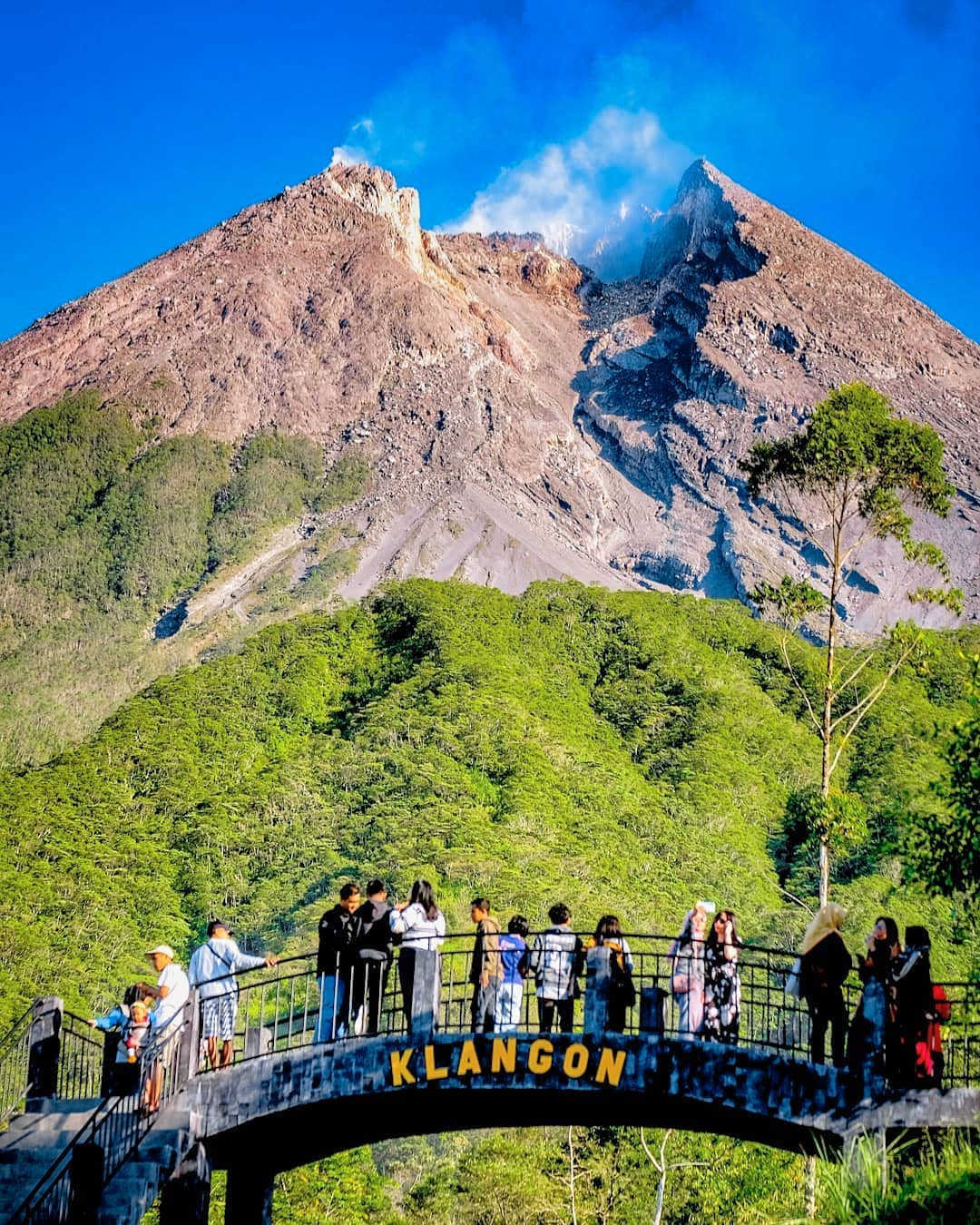 Visitors standing on an observation platform at Klangon Hill with Mount Merapi in the background under a clear blue sky.