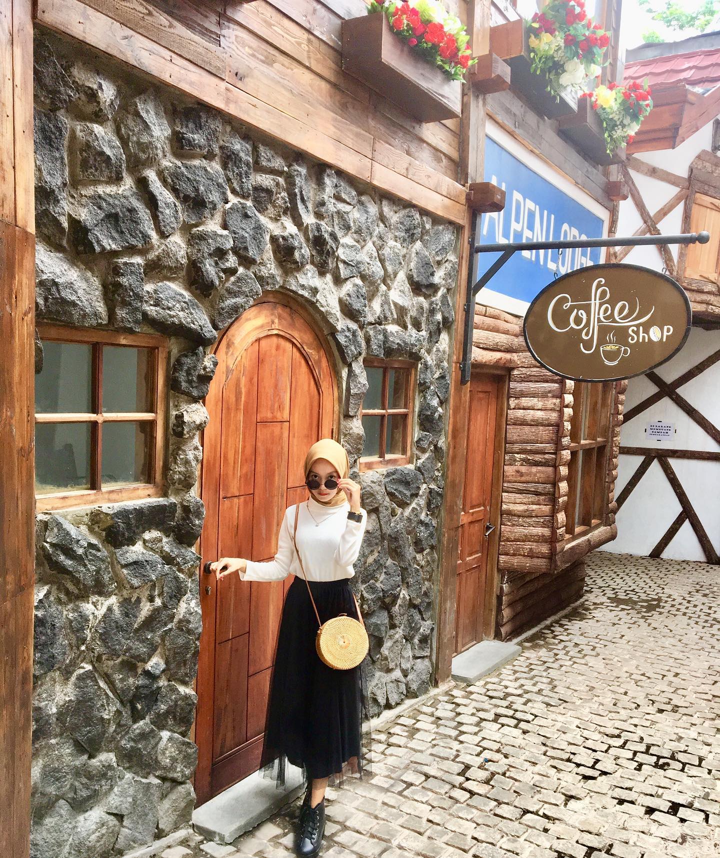 A woman standing in front of a rustic stone and wood building with a coffee shop sign at Bhumi Merapi Agrotourism.