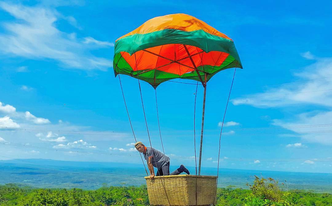 A person posing in a hot air balloon-inspired photo spot at Mount Mungker with a scenic view in the background.