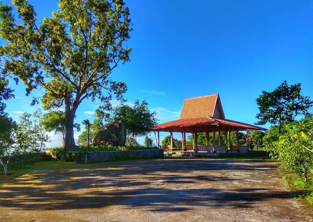 A traditional joglo pavilion surrounded by trees and greenery under a clear, blue morning sky at Gunung Gambar.