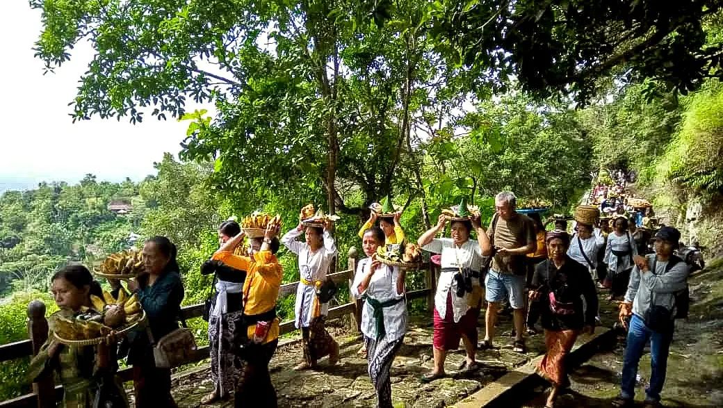 A group of people, part of the Hindu community in Gunungkidul, participate in the Merti Gunung ceremony at Gambar Mountain, carrying offerings on their heads.