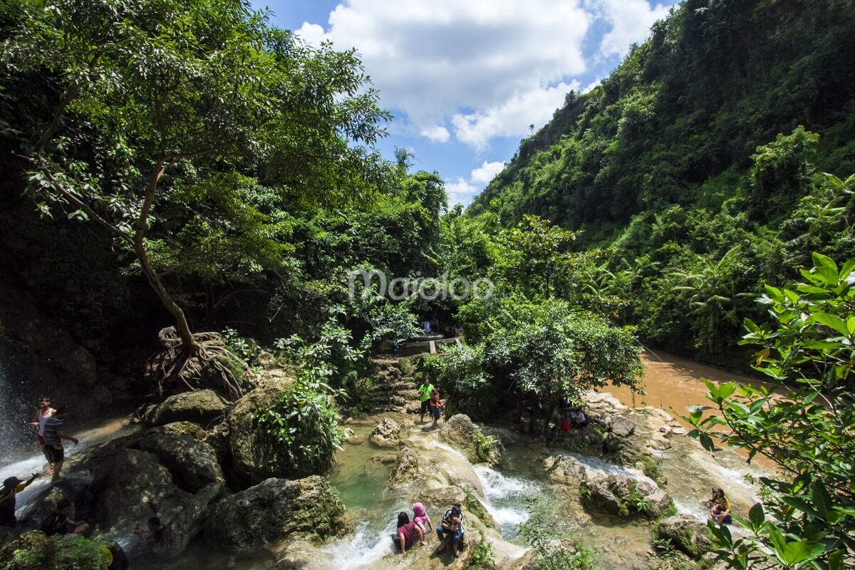 Beautiful view of the lush green surroundings and visitors enjoying the natural pools and Oyo River near Sri Gethuk Waterfall in Yogyakarta, Indonesia.