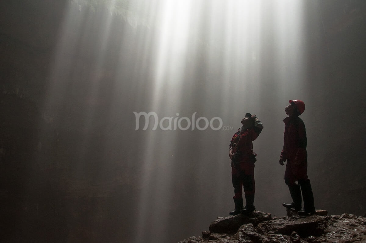 Two cavers admiring beams of light streaming into Grubug Cave.