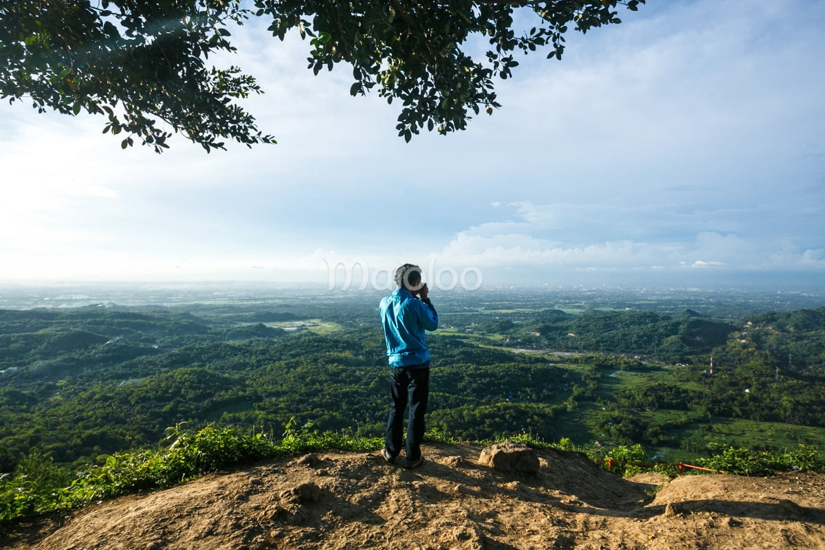 A visitor in a blue jacket takes a photo of the vast landscape from Becici Peak.