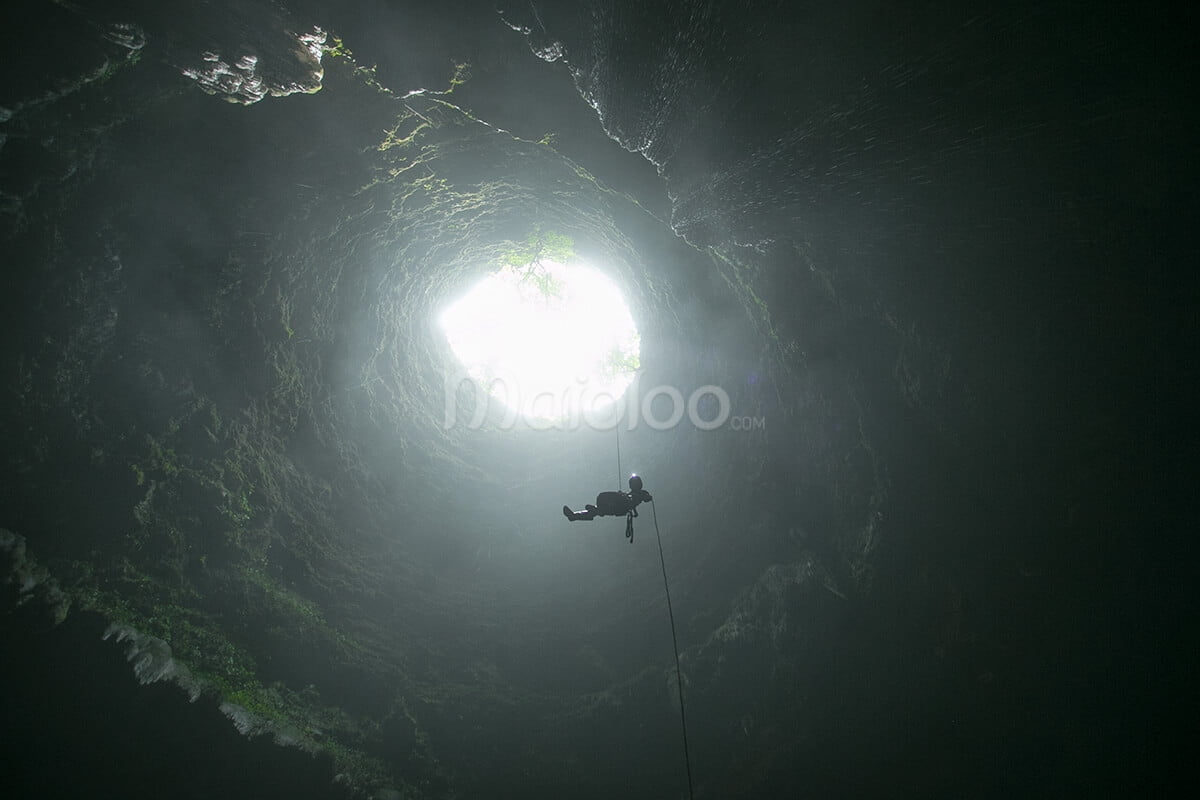 Caver using a single rope technique to descend from the entrance of Grubug Cave.