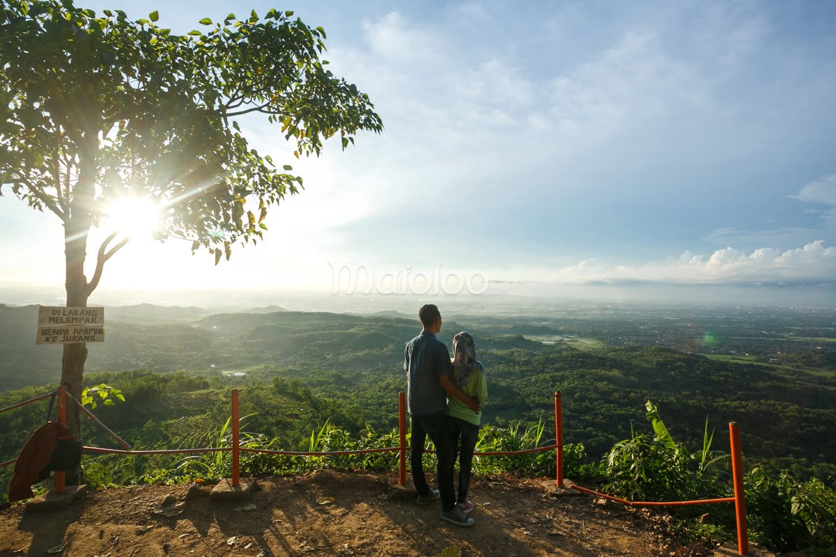 A couple stands together, enjoying the expansive view from Becici Peak during a clear sunset.