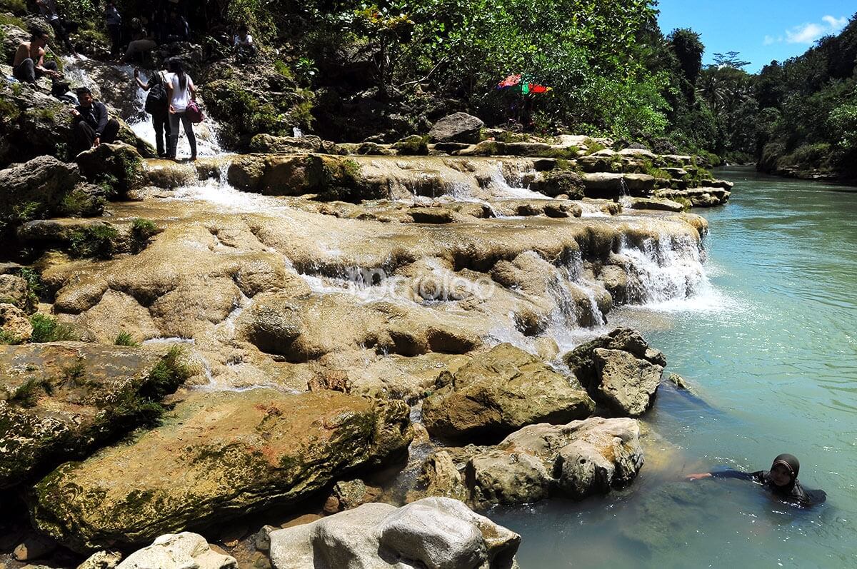 People enjoying the karst rock formations and swimming at Sri Gethuk Waterfall in Yogyakarta, Indonesia.