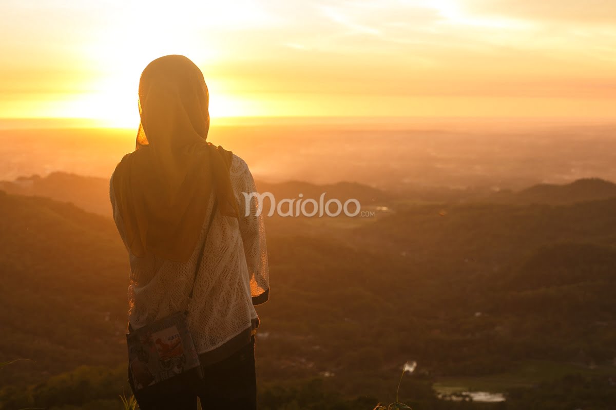 A woman in a headscarf enjoys the golden sunset view over the landscape from Becici Peak.