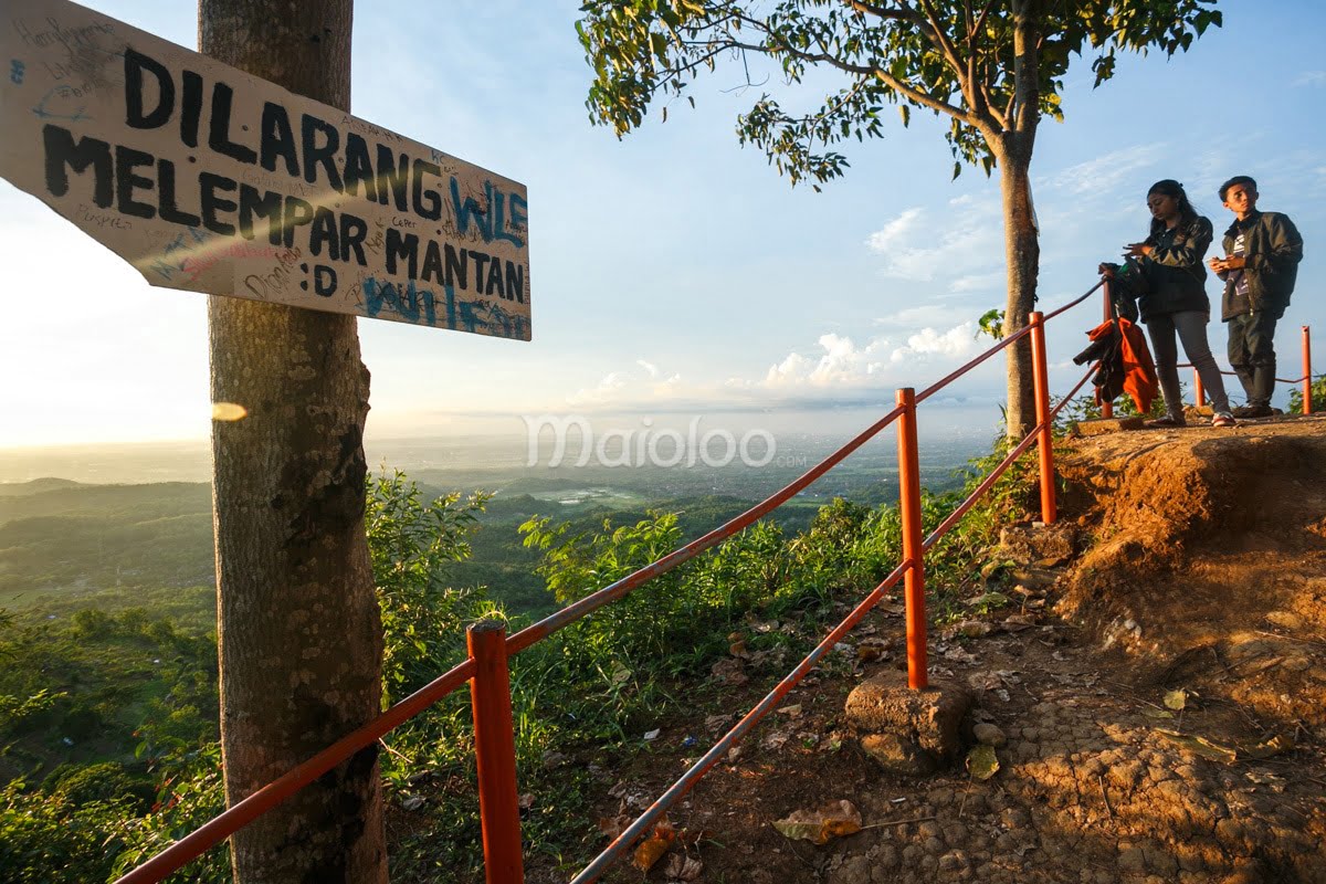 A humorous sign at Becici Peak warns against throwing exes, with visitors enjoying the view of the surrounding landscape.