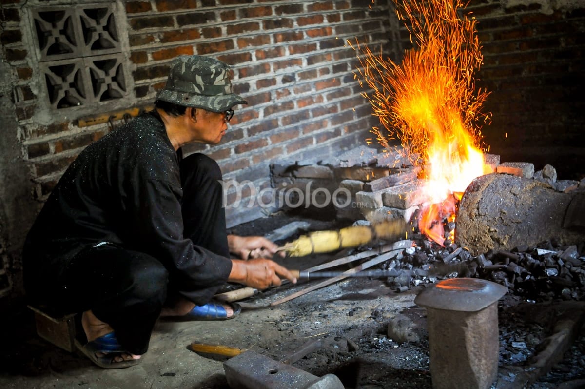 Craftsman tending to the embers in a traditional forge to keep the temperature high.