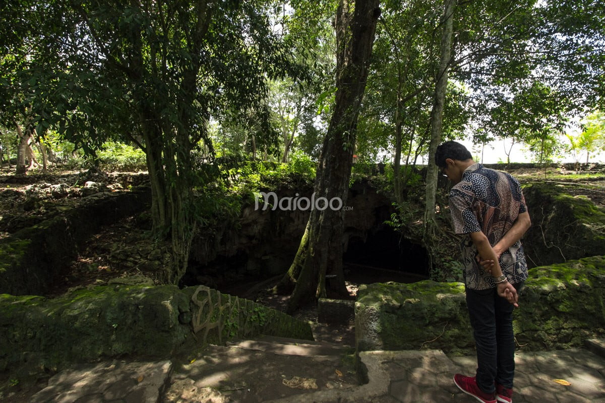 A person looking down into the entrance of Rancang Kencono Cave surrounded by lush greenery.