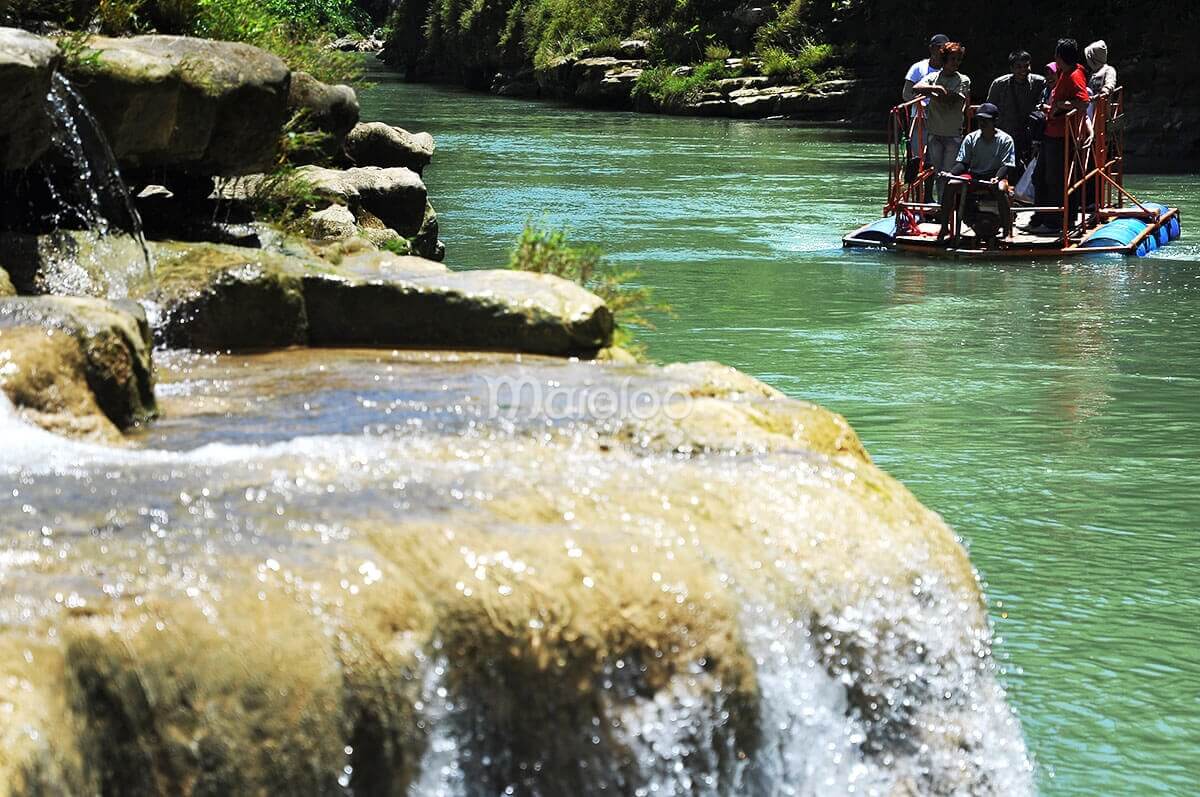 Visitors using a local raft to access the main area of Sri Gethuk Waterfall in Yogyakarta, Indonesia.