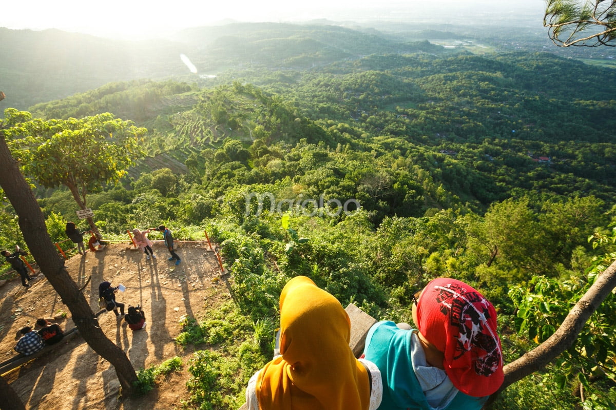 A group of visitors gathers on a viewpoint at Becici Peak, enjoying the scenic landscape and lush green forests.