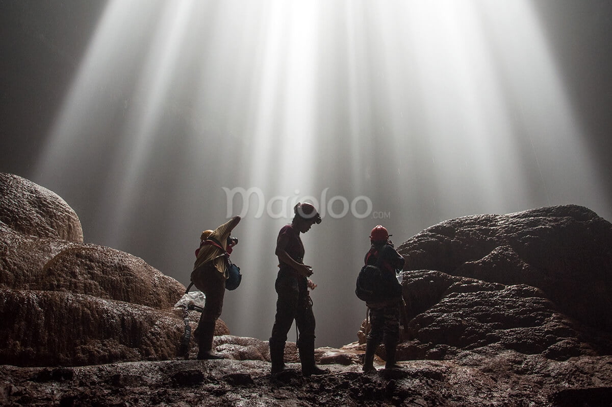 People standing in Grubug Cave, illuminated by beams of sunlight streaming through the cave opening.