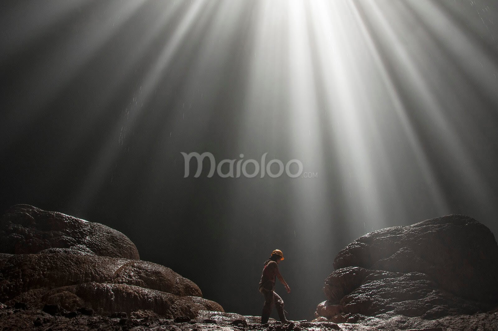 A person walking in Grubug Cave, illuminated by dramatic beams of sunlight.