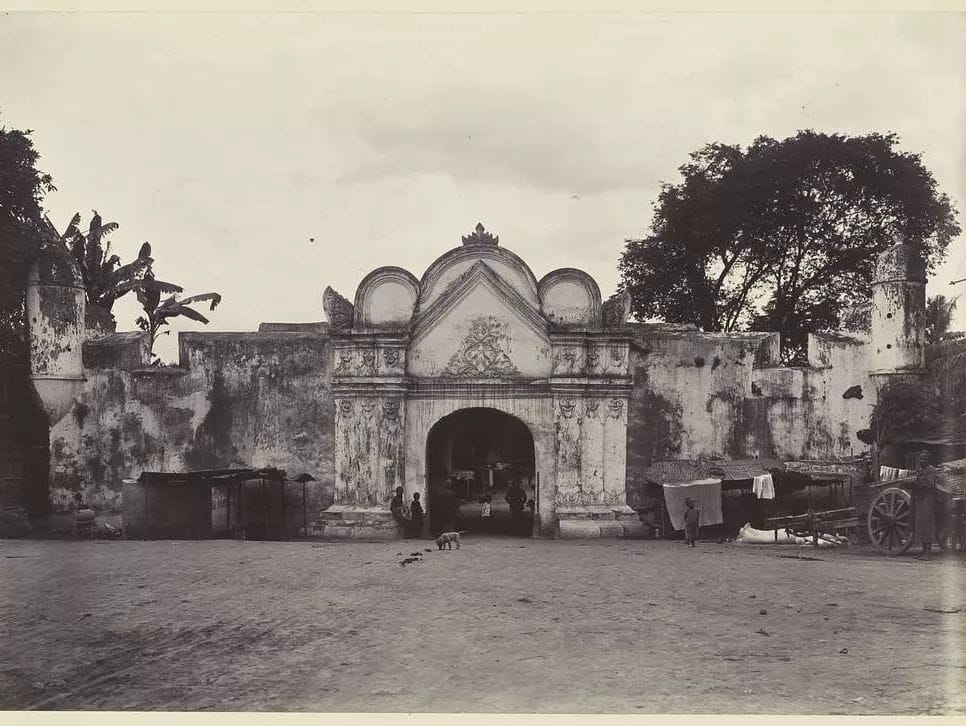 A black-and-white photo of Plengkung Jagasura, the northern gate of Yogyakarta Palace's fortress, taken in 1900. The ancient, ornate gate is surrounded by thick fortress walls with a group of people and carts visible in the foreground.