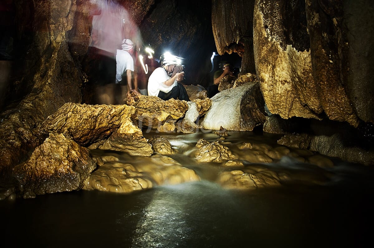 People photographing the intricate rock formations and flowing water inside Cerme Cave.