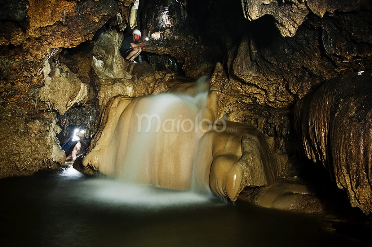 Stunning waterfall inside Cerme Cave with explorers shining lights.