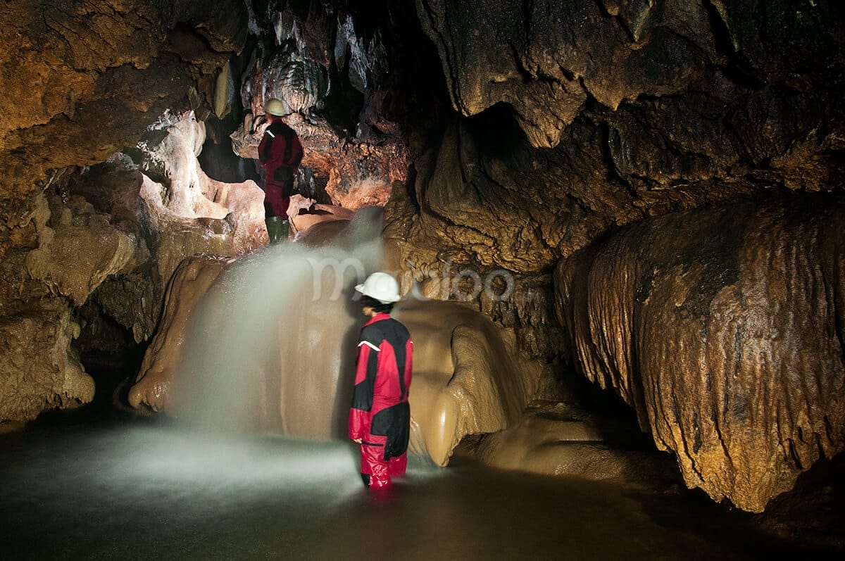 Adventurers exploring the stunning interior of Cerme Cave with waterfalls and limestone formations.