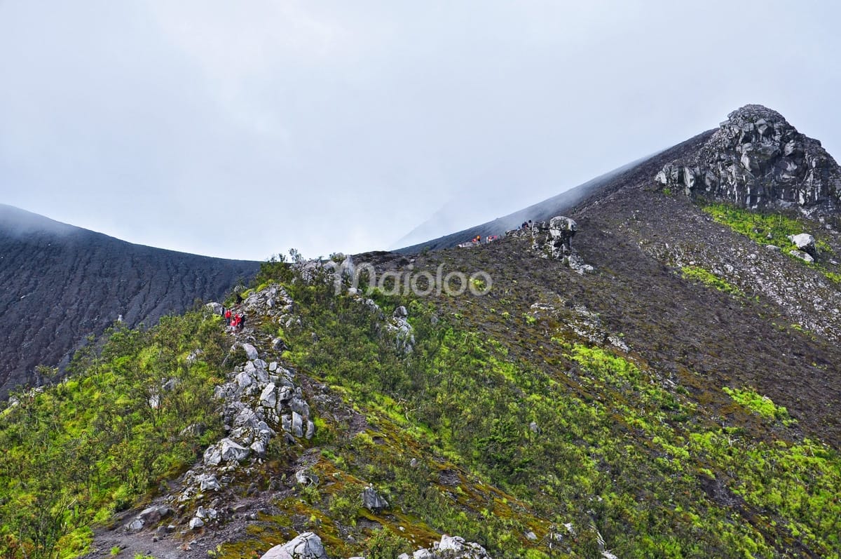 Hikers walking on a rocky ridge trail after Watu Gajah, nearing the Pasar Bubrah area of Mount Merapi.