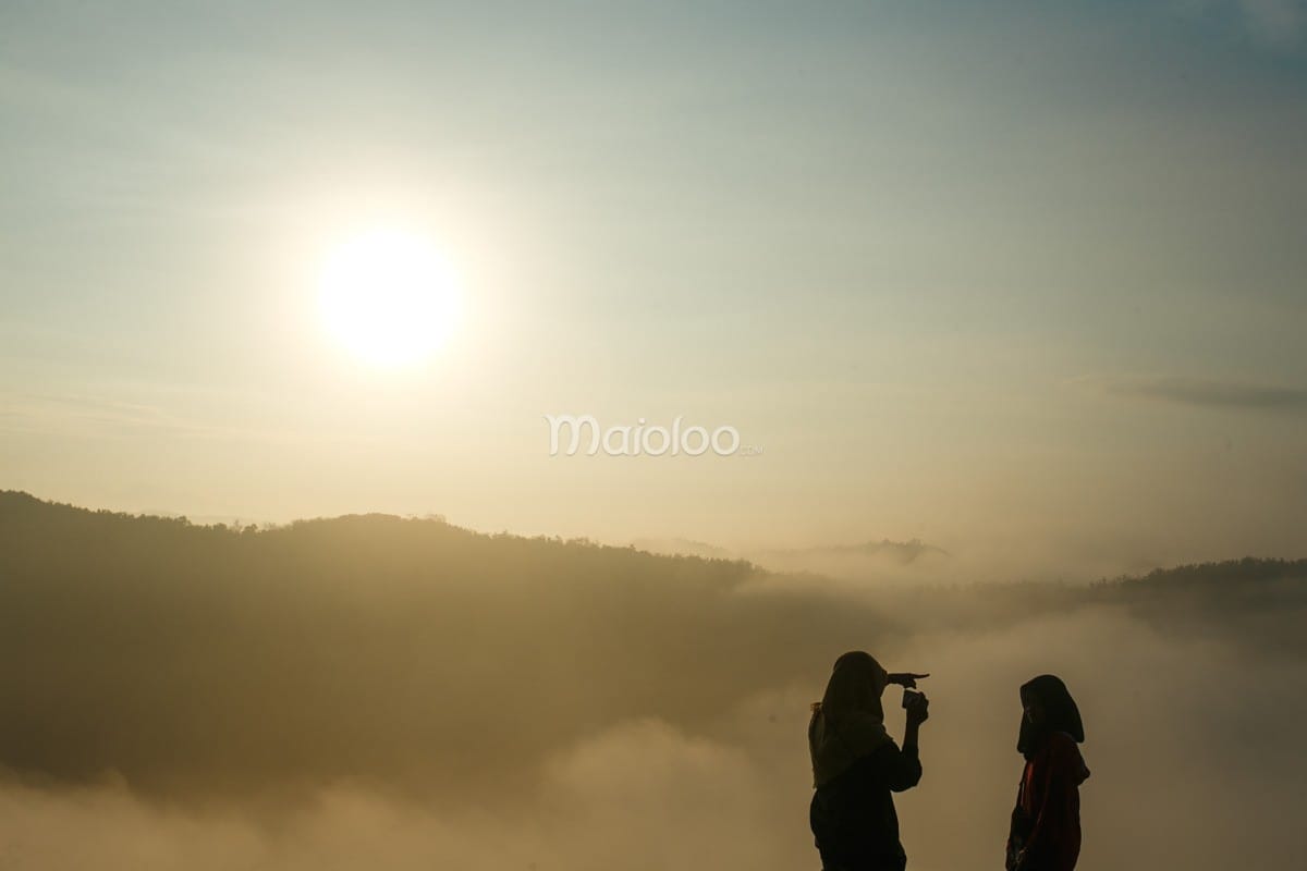 Two people enjoying the sunrise over a sea of clouds at Panguk Kediwung Hill.