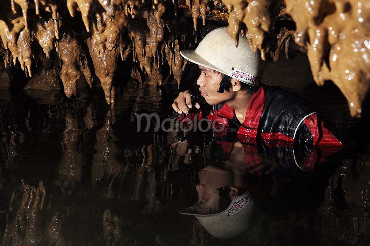 Explorer crouching under low stalactites in Cerme Cave.