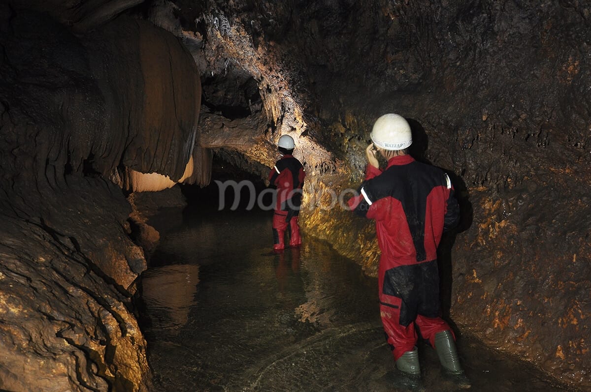 Explorers wearing safety gear wade through the watery passages of Cerme Cave.