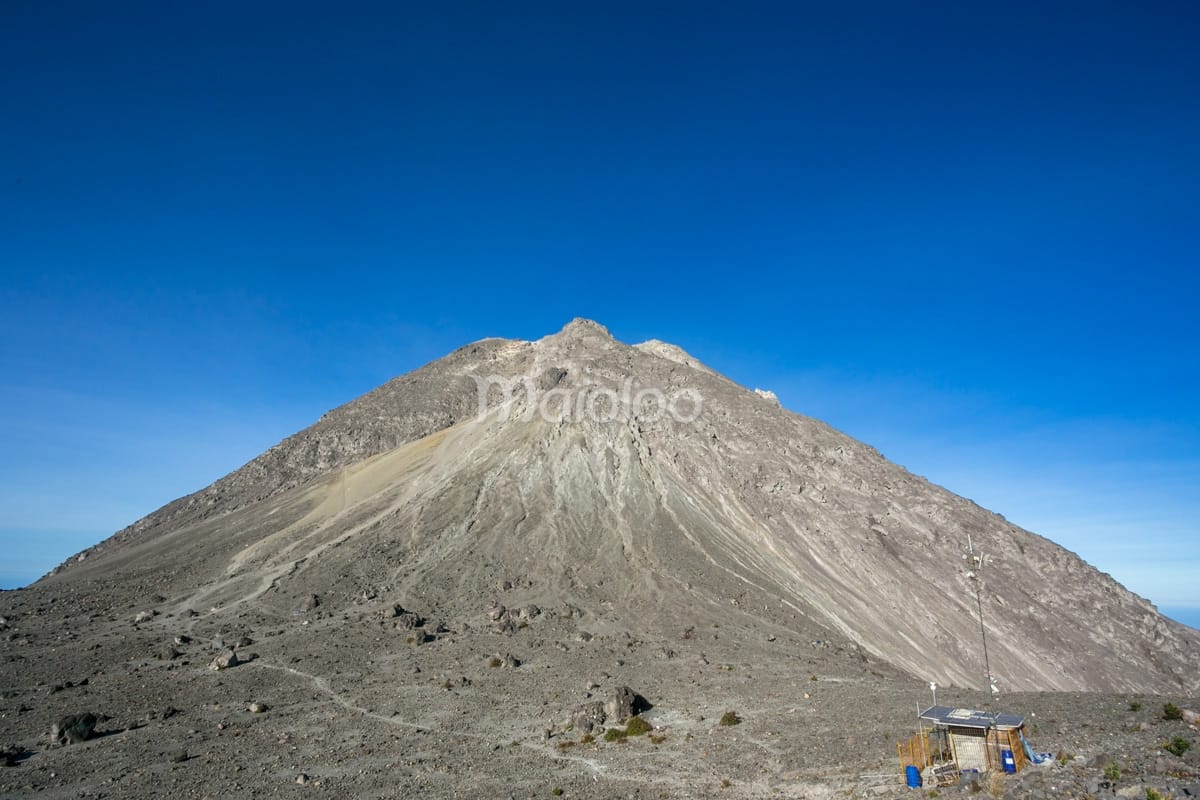 View of Pasar Bubrah at the base of Mount Merapi's rocky summit under a clear blue sky.