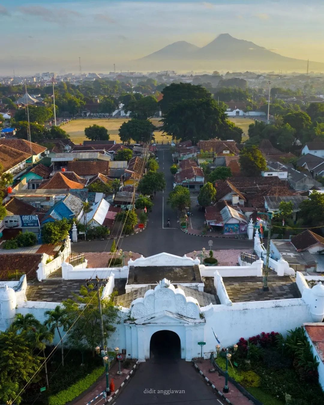 An aerial view of Plengkung Gading, the historical southern gate of Yogyakarta Palace. The surrounding area includes residential houses, trees, and distant mountains under the morning light.