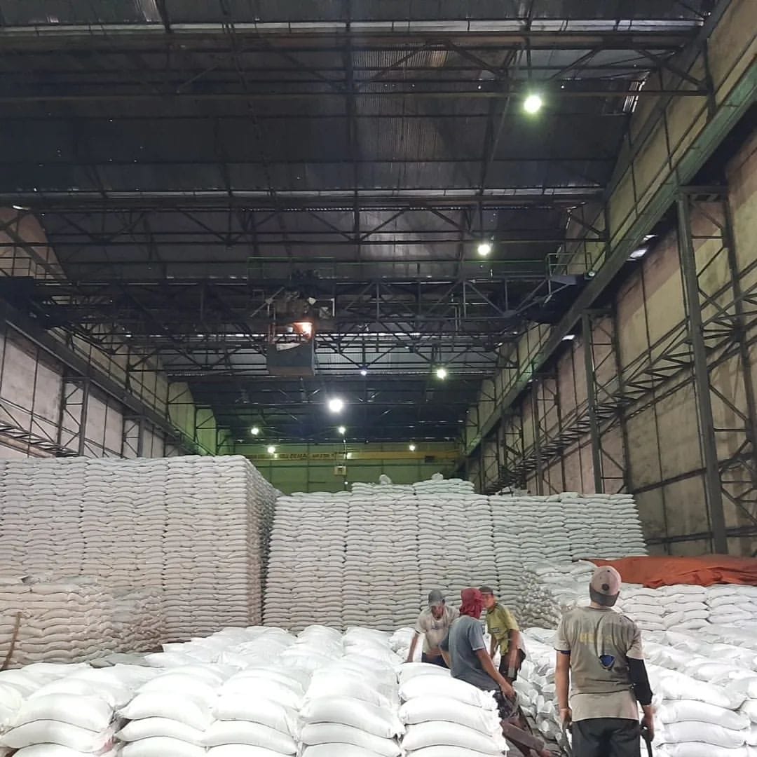 Workers organizing large stacks of white sugar sacks in a warehouse at Madukismo Sugar Factory.