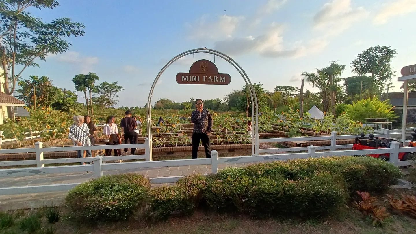 Visitors exploring the Mini Farm at Obelix Village, Yogyakarta, surrounded by neatly arranged plant beds, flowers, and greenery under a clear blue sky.