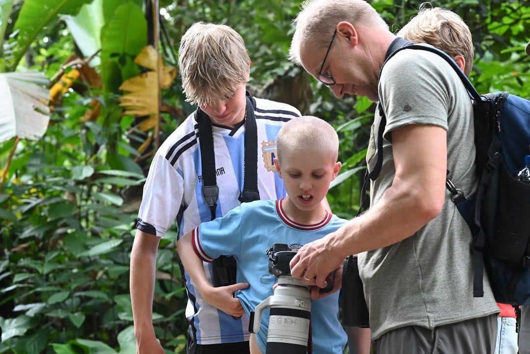 A group of tourists reviewing bird photographs on a camera in the lush greenery of Wanagama Forest.