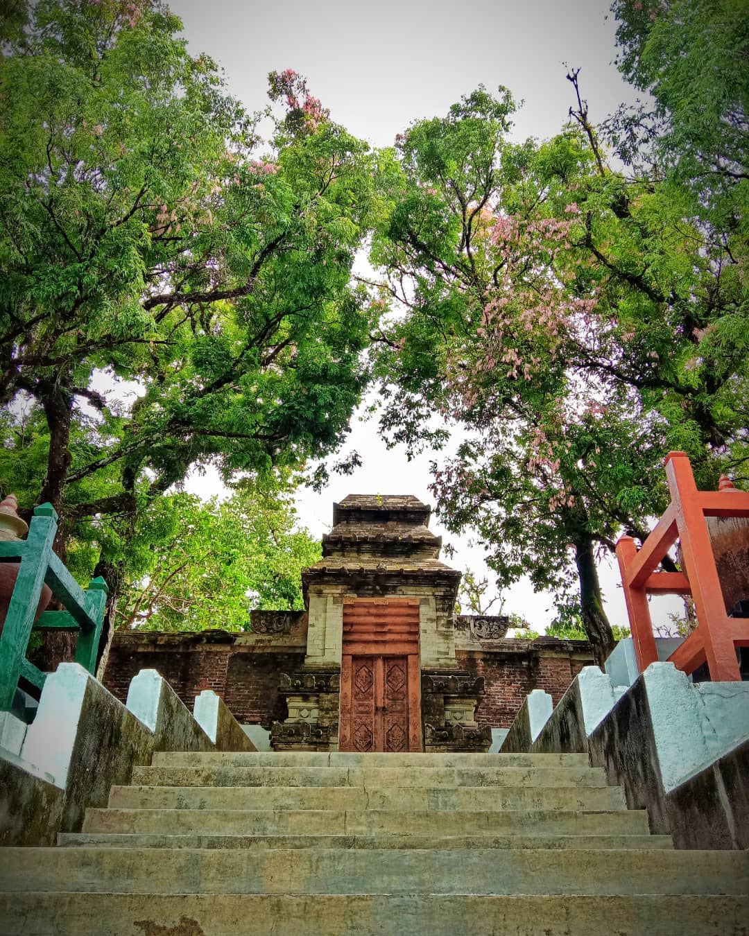 Stone steps leading up to a traditional Javanese gate at Imogiri Royal Cemetery, surrounded by lush green trees.