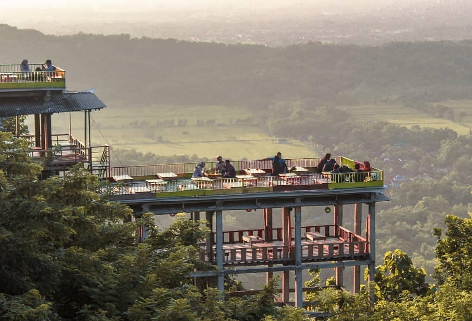 Visitors enjoying the scenic view of the valley from an elevated café on Bukit Bintang, surrounded by greenery during the day.