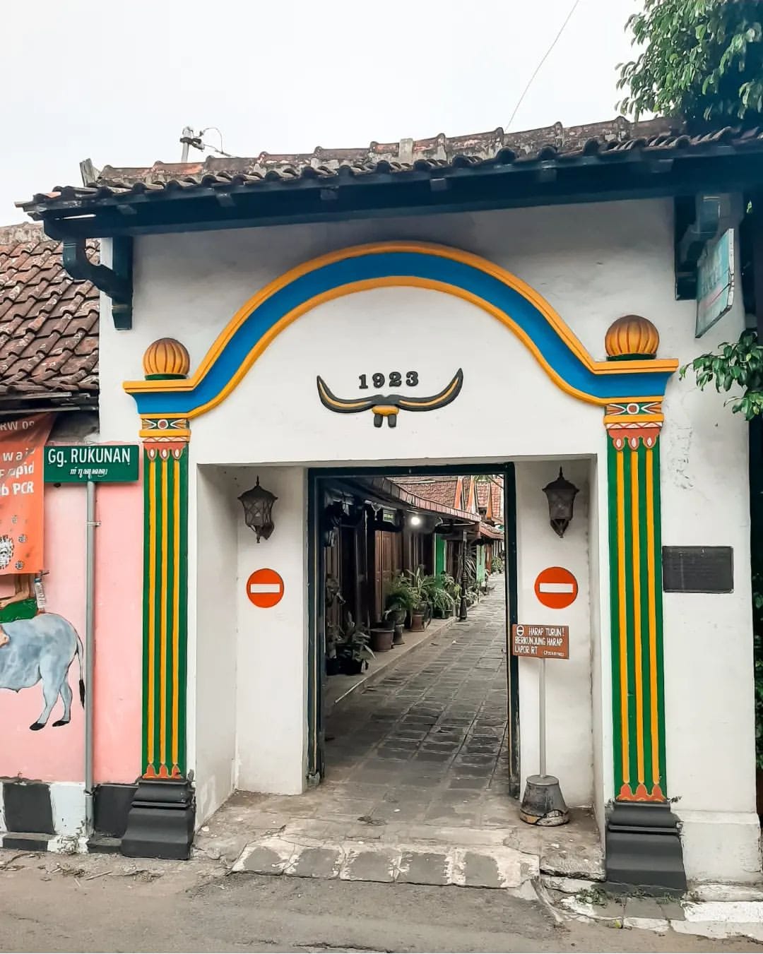 A colorful gate from 1923 in Kotagede, featuring bright yellow and blue accents with a narrow alley visible through the entrance.