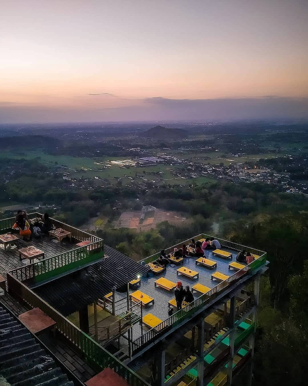 People sitting at an outdoor café on Bukit Bintang, enjoying the panoramic view of the valley below during sunset.