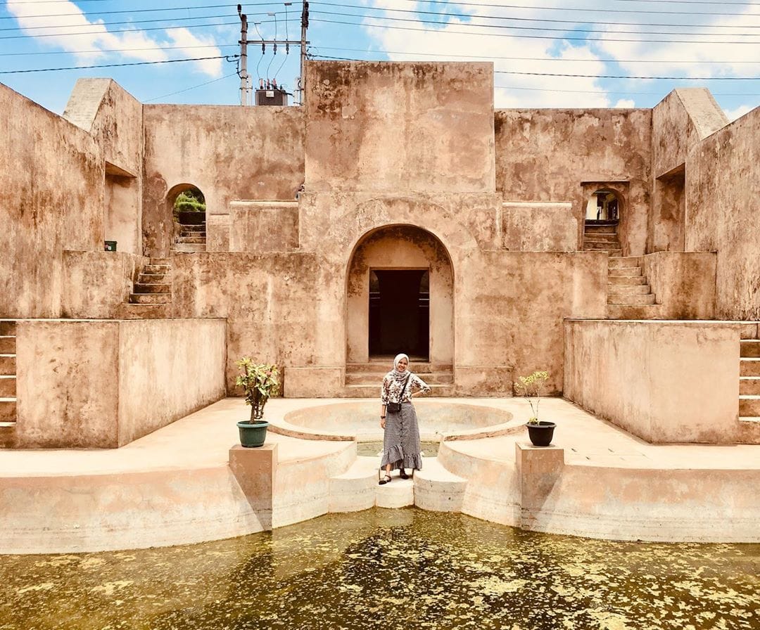 A visitor poses near the iconic central pool at Warungboto Site in Yogyakarta, surrounded by ancient stone structures and bright blue skies.