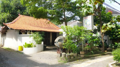 The entrance to Cemeti Art House, a contemporary art space in Yogyakarta, with a traditional building and sculptures surrounded by trees and greenery.