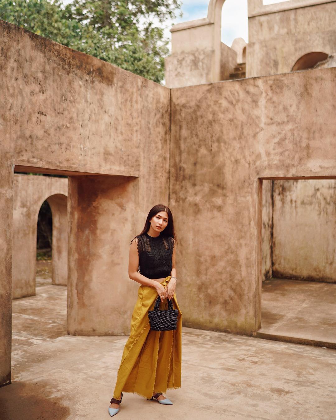 A woman poses stylishly in a vibrant outfit at Warungboto Site in Yogyakarta, with its rustic stone walls and arches creating a photogenic backdrop.